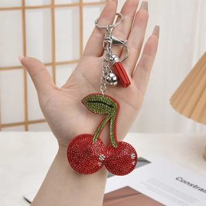 Detailed shot of cherry rhinestone keychain with red tassels and metal bell held by hand