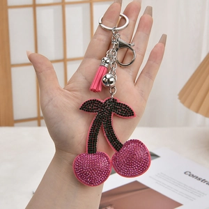 Pink cherry rhinestone keychain with leather tassel and silver bell held by hand