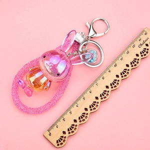 Detailed macro view of a pink acrylic bunny keychain with glitter strap on pink backdrop