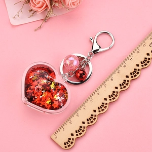 Macro shot of heart-shaped acrylic oil keychain with red glitter and pink bell accessory