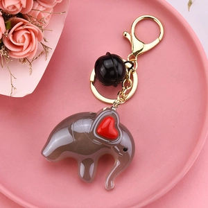 Gray acrylic elephant keychain with red heart detail and black bell on pink tray