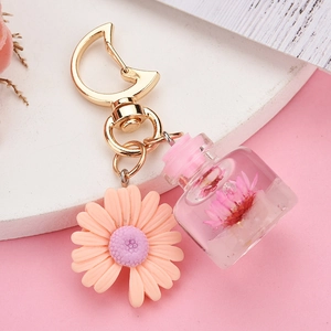 Macro view of moon-shaped gold buckle with pink daisy and preserved flower bottle keychain