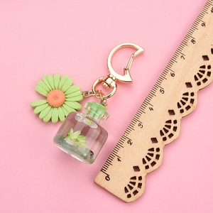 Detail of daisy keychain with mini glass bottle and golden moon clasp over pink backdrop