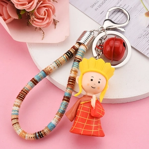 Close-up of a cartoon monk keychain with red robe, woven strap and metal bell accessory
