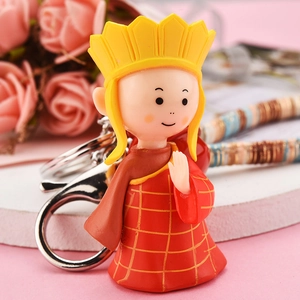 Cute chibi monk keychain with yellow crown and red robe on a pink floral background