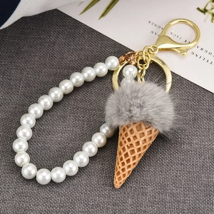 Close-up of grey mink fur ice cream keychain with white pearls on a woven texture