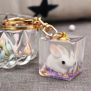 Macro shot of 3D white rabbit inside a clear resin cube keychain with gold glitters