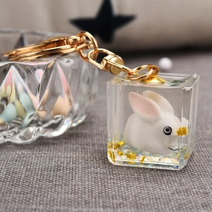 Detail of cubic resin keychain with white rabbit and gold leaf inside on grey fabric