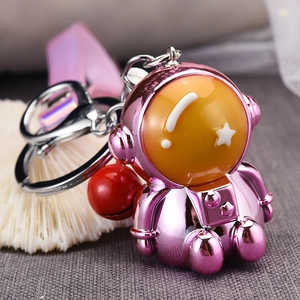 Close-up of metallic pink astronaut keychain with red bell and pink wrist strap accessory