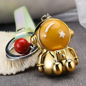 Detailed view of a shiny gold astronaut keychain with a red bell and iridescent strap