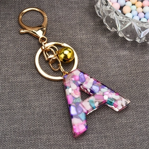Detail of letter A resin keychain with colorful stones and a small gold bell charm
