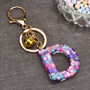 Detail view of resin letter D keychain with colorful stones, gold ring and small bell