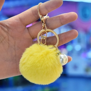 Detail of yellow faux fur pompom keychain with golden clasp and large pearl accent