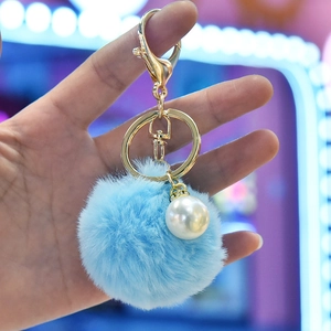 Detail of light blue faux rabbit fur pom pom keychain with a large white pearl and gold clasp