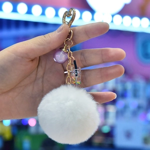 Detail of fluffy white fur pompom keychain with purple bead and heart-shaped gold clasp