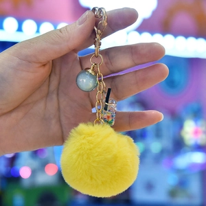 Detail of yellow faux fur pom pom keychain with gold heart clasp and mini drink charm