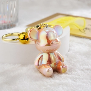 Macro detail of iridescent bear keychain with gold bell and yellow silicone strap