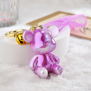 Iridescent cartoon bear keychain with purple gradient, golden bell, and violet wrist strap