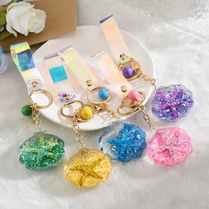 Sparkly acrylic seashell oil-filled keychains in five colors on a white ceramic tray