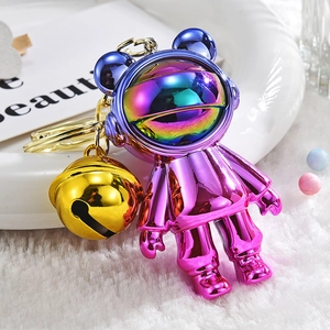 Close-up of purple gradient astronaut bear keychain with gold bell on white plush