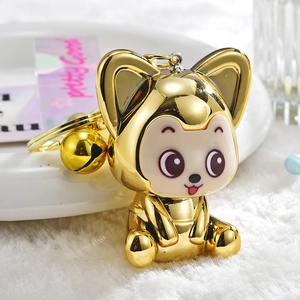 Close-up of a gold-plated fox keychain with a small bell on a white textured background