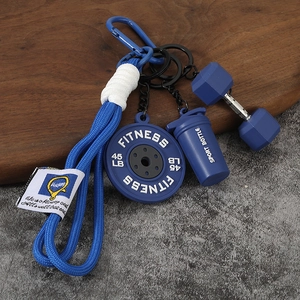 Détail d'un porte-clés fitness avec disque d'haltère bleu, shaker et haltère sur bois