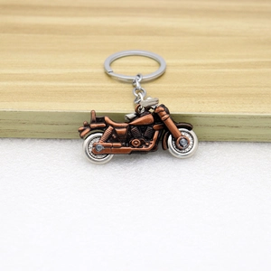 Vintage motorcycle keychain with bronze alloy body and movable silver wheels on wood surface