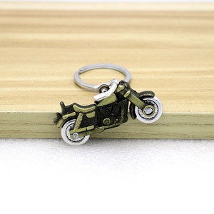 Retro bronze motorcycle keychain with movable wheels on a light wooden display stand