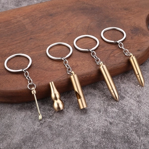 Brass keychain set with bullet and whistle pendants on a wooden tray with a grey background