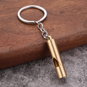 Polished brass whistle keychain with silver split ring on textured stone background