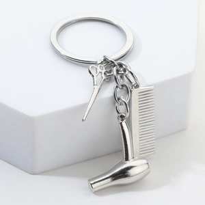 Porte-clés coiffeur avec breloques ciseaux, peigne et sèche-cheveux sur socle blanc