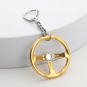 Steering wheel metal keychain with gold and silver dual-tone finish on a white stand