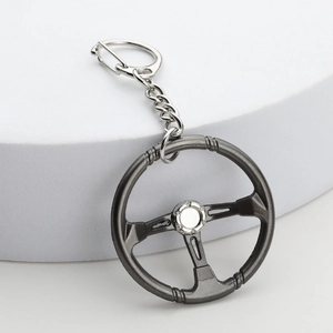Close-up of a mini 3-spoke racing steering wheel keychain on a white pedestal