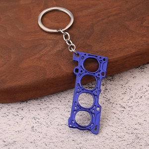 Blue zinc alloy car engine cylinder head gasket keychain on dark textured background