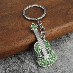 Polished silver guitar keychain with sparkling green rhinestones on dark wood background