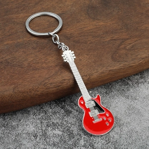 Detail of a red electric guitar keychain with polished metal finish on rustic wood
