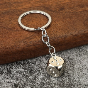Macro detail of silver zinc alloy dice keychain with sparkling crystals on a wooden base
