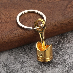 Creative gold car engine piston keychain with polished metallic finish on stone surface