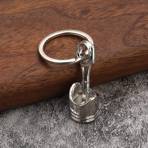 Polished silver metal engine piston keychain with connecting rod on stone surface