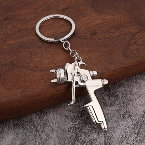 Silver zinc alloy spray gun keychain with realistic details on wood and stone background