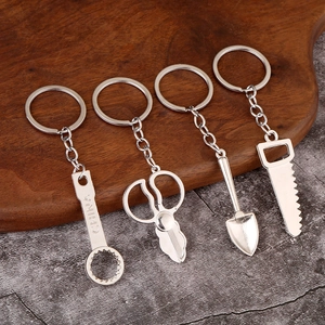 Miniature silver metal tool keychain set including wrench, scissors and shovel on wood surface