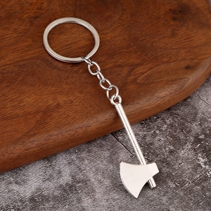 Detailed close-up of a silver metal axe tool keychain on a dark wooden and stone background