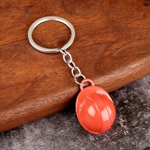 Mini orange safety helmet keychain with a shiny finish on a rustic wooden background