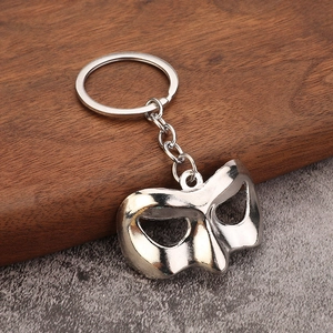 Polished silver metal half-face phantom mask keychain on a rustic wooden background