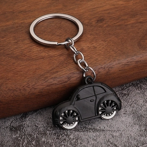 Vintage matte black beetle car keychain with silver wheels on a textured background
