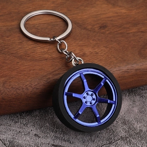 Blue six-spoke car wheel rim keychain with black tire on a rustic textured surface
