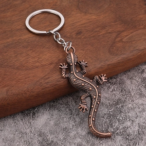 Porte-clés gecko vintage avec écailles cuivrées sur un fond rustique en bois et pierre