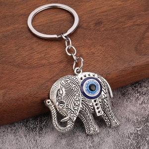 Vintage silver elephant keychain with blue evil eye bead on a rustic wooden background