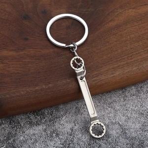 Miniature silver metal wrench keychain tool with industrial matte finish on a wooden base