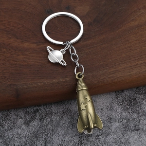 3D metallic rocket and Saturn planet keychain pendant on textured wooden background